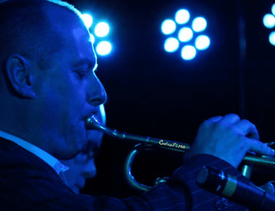 A musician plays a trumpet infront of blue stage lights