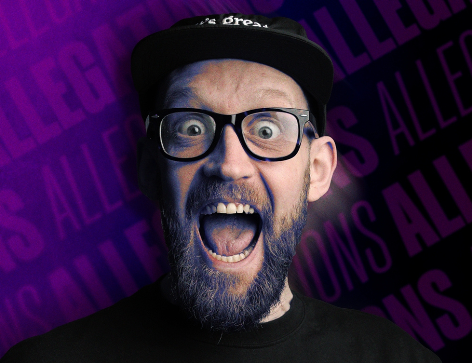 An image of a man in a dark cap, with a beard and glasses 'shouting' toward the camera